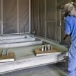 Dans cabine de sablage, opérateur avec lance de sablage